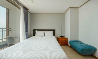 A hotel room with a bed, a nightstand, a blue chair, and a window with curtains.