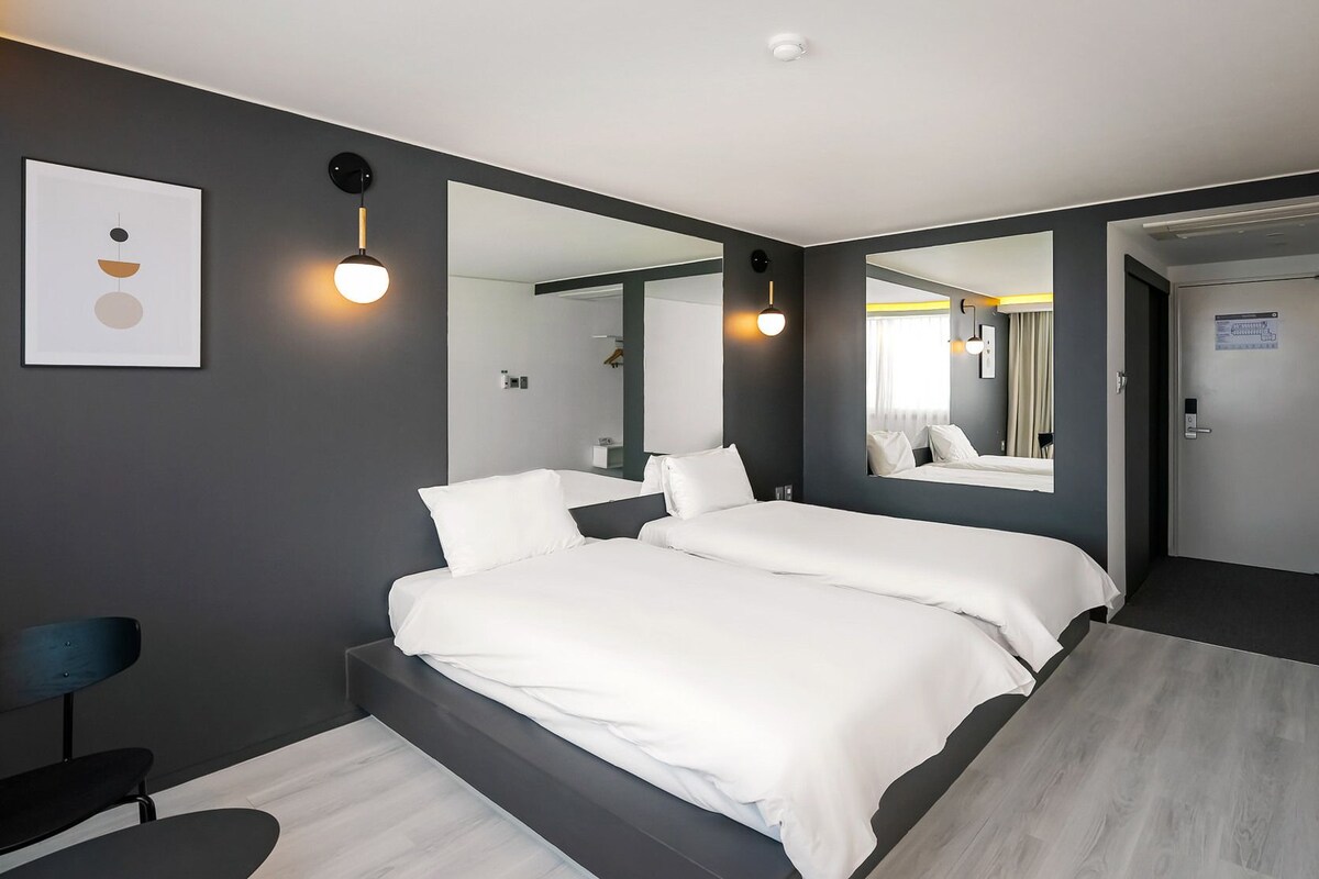 Ein modernes Hotelzimmer mit einem großen Bett, einem Sessel, einem Schreibtisch und einem Spiegel.
