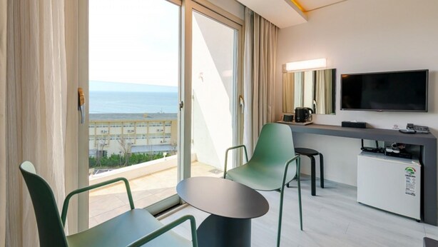 A modern hotel room with a balcony, a flat-screen TV, a small table, and a desk with a coffee machine. - Pampas Hotel Jeju (Jeju City)
