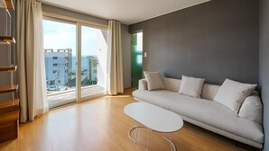 A modern living room with a grey sofa, a white coffee table, and a view of the city through large windows. - Pampas Hotel Jeju (Jeju City)