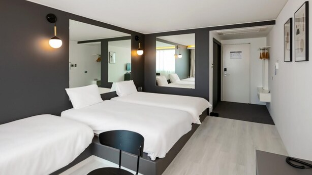Une chambre d’hôtel moderne avec un grand lit, un petit bureau, un miroir et une salle de bain visible à travers une porte ouverte.