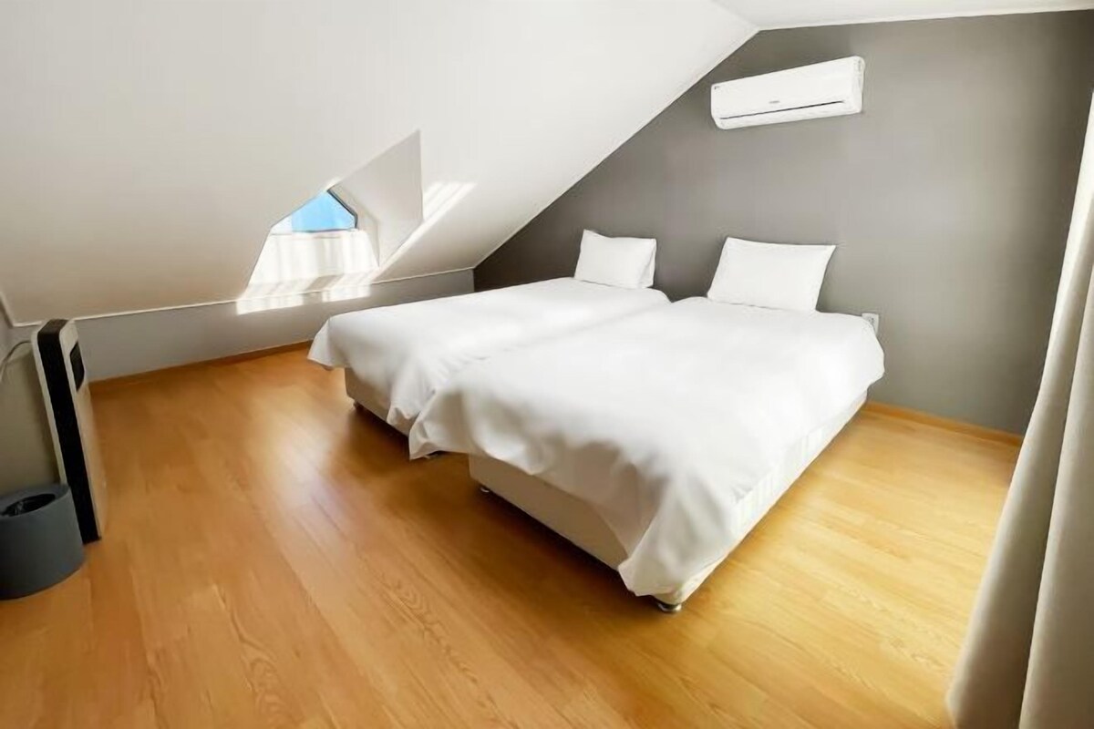 Ein modernes Schlafzimmer mit schrägem Dach, Oberlicht, Bett mit weißer Bettwäsche und einer grauen Wand.
