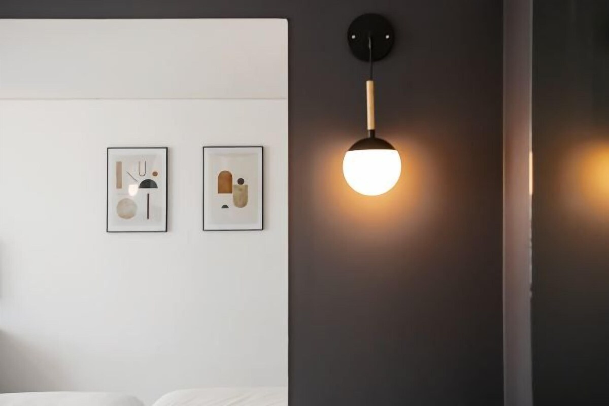 Ein modernes Schlafzimmer mit einem Bett, einer Wandleuchte und zwei gerahmten Kunstwerken.