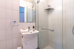Een moderne badkamer met een douchecabine van glas, een witte wastafel en een spiegel.