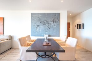 Een moderne eethoek met een donker houten tafel, twee witte fauteuils en een groot abstract schilderij aan de muur.