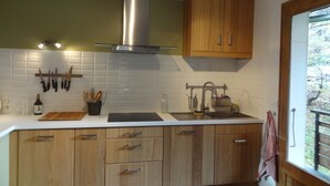 Une cuisine moderne avec des meubles en bois, une hotte de cuisine en acier inoxydable et une fenêtre donnant sur un paysage verdoyant.