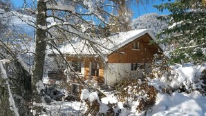 Une cabane en bois entourée d’arbres couverts de neige, sous un ciel bleu et dégagé.