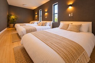 A hotel room with three beds, a large window, and a potted plant.