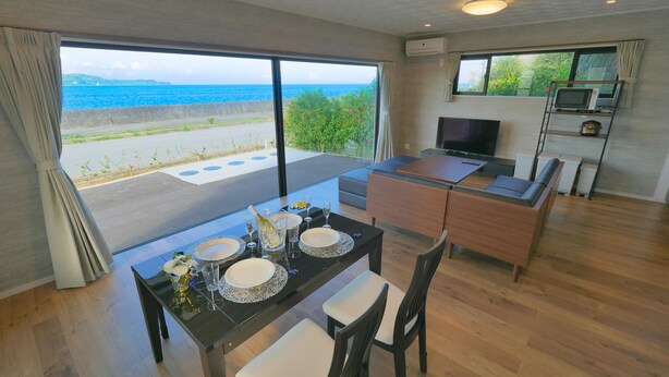Uma área de refeições com vista para o mar, uma TV e uma cozinha compacta.