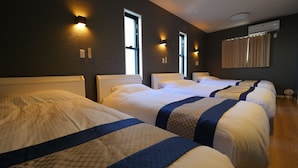 Quarto de hotel com quatro camas, cada uma com cabeceira e mesa de cabeceira. Há luminárias fixadas na parede e um aparelho de ar condicionado.