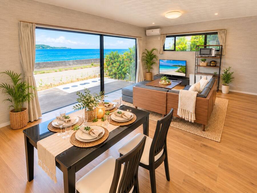 Una sala de estar moderna con un televisor grande, un comedor con una mesa dispuesta para cuatro personas, y vista al océano a través de amplias ventanas.