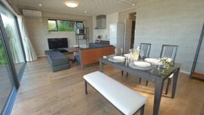 Uma sala de estar moderna com um sofá, uma mesa de jantar posta para quatro e uma televisão.