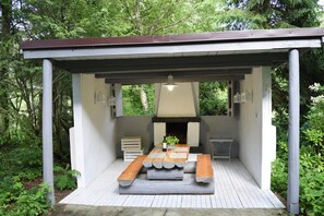 A covered outdoor seating area with a table and benches, surrounded by greenery. - Large holiday home, summer pool, sauna, whirlpool (Sasino)