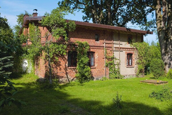 A brick building with a sloped roof, surrounded by lush greenery and trees. - Large holiday home, summer pool, sauna, whirlpool (Sasino)