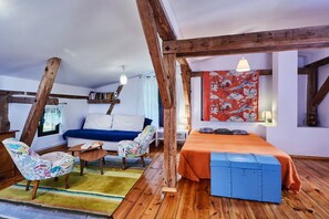 A room with a wooden ceiling, a blue sofa, a bed with an orange bedspread, a blue chest of drawers, and a colorful chair. - Large holiday home, summer pool, sauna, whirlpool (Sasino)
