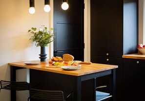 A dining area with a wooden table, black chairs, a vase with green plants, and a plate of food.