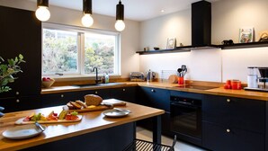 A modern kitchen with a wooden countertop, a built-in oven, and a window providing natural light. - The West Nest -Luxury Cottage, Sea Views & Hot Tub (Isle of Skye)