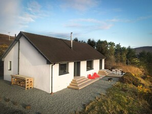 A single-story house with a sloped roof, a chimney, and a gravel driveway.