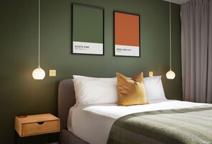 Ein Hotelzimmer mit einem Bett, zwei Wandleuchten, einem Nachttisch und zwei gerahmten Farbmustern an der Wand.