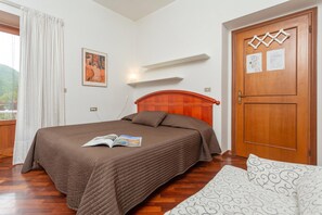 Een slaapkamer met een houten bed, een raam met gordijnen, een wandplank en een deur met papieren.