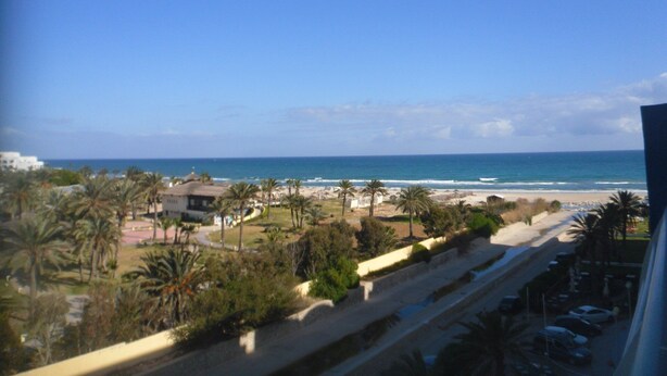 A coastal view with a beach, palm trees, and a road leading to a parking area. - S+1 in the tourist zone (Sousse)
