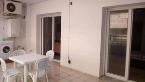 A room with a white table and chairs, a washing machine, and a sliding glass door leading to an outdoor area. - S+1 in the tourist zone (Sousse)