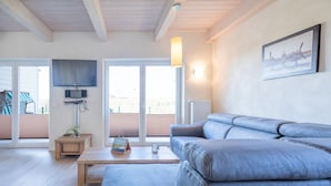 A modern living room with a blue leather sofa, a wooden coffee table, and a flat-screen TV mounted on the wall.