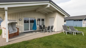 A covered patio area with a table and chairs, a striped bench, and two lounge chairs.