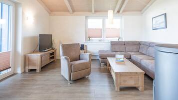 Ein Wohnzimmer mit Sofa, Sessel, Couchtisch, Fernseher und Heizkörper.