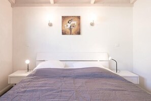 Une chambre à coucher comprenant un lit, deux tables de chevet, une commode, une œuvre d’art accrochée au mur et un luminaire fixé au plafond.