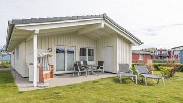 Einbungalow mit einer überdachten Terrasse, einem Essbereich mit Tisch und Stühlen sowie einem kleinen Garten.