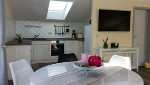 A modern kitchen with white cabinets, a built-in oven, and a microwave. There's a dining table with chairs and a TV mounted on the wall. - "Kleine Auszeit" Helle Ferienwohnung mit Balkon, mitten im Zentrum (Burg (Spreewald))