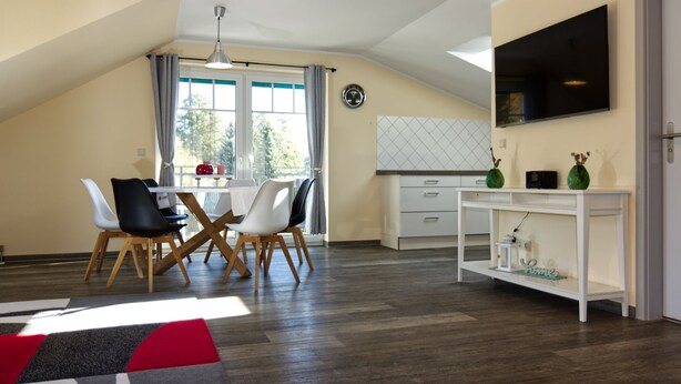 A modern kitchen with a dining area, wooden flooring, and a TV mounted on the wall. - "Kleine Auszeit" Helle Ferienwohnung mit Balkon, mitten im Zentrum (Burg (Spreewald))