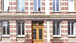 A building with a symmetrical facade, featuring a central wooden door with decorative glass panels, flanked by windows with metal bars. - Apartment in Normandy near Pebble Beach (Fécamp)