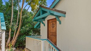 Une porte en bois ornée d’une grille métallique décorative, une balustrade de porche blanche et une structure de toit de couleur turquoise.