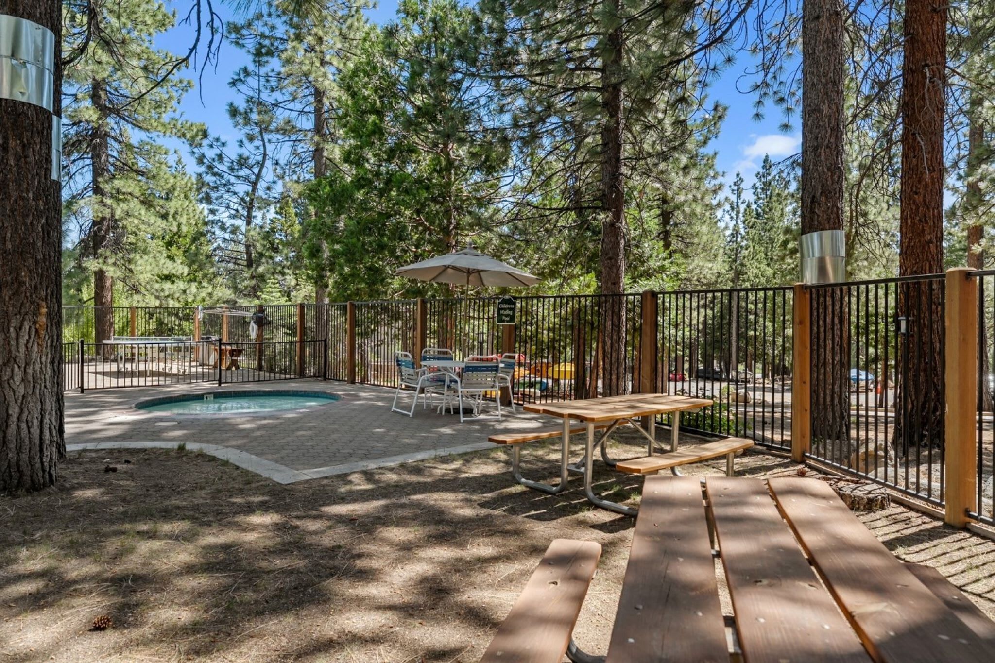 A fenced outdoor area with a pool, picnic tables, and chairs.