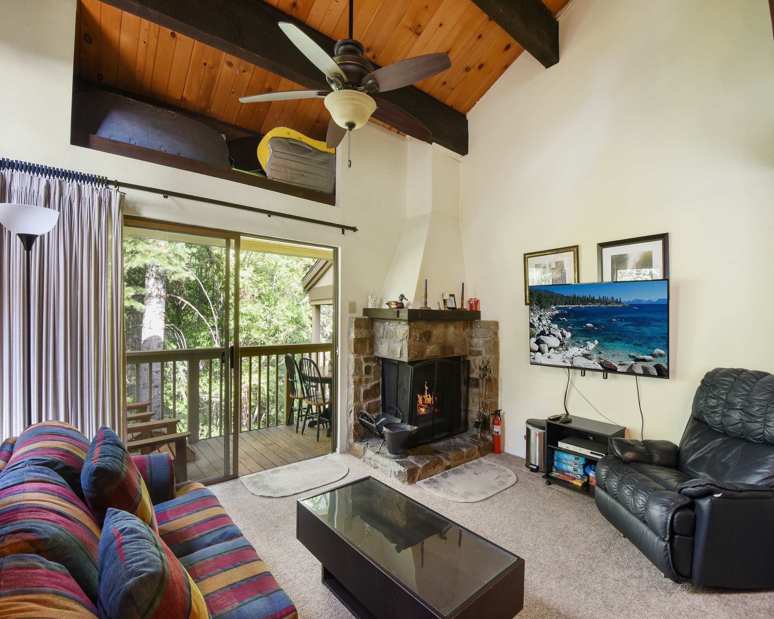 A cozy living room with a fireplace, a ceiling fan, a large window, and a black leather sofa.