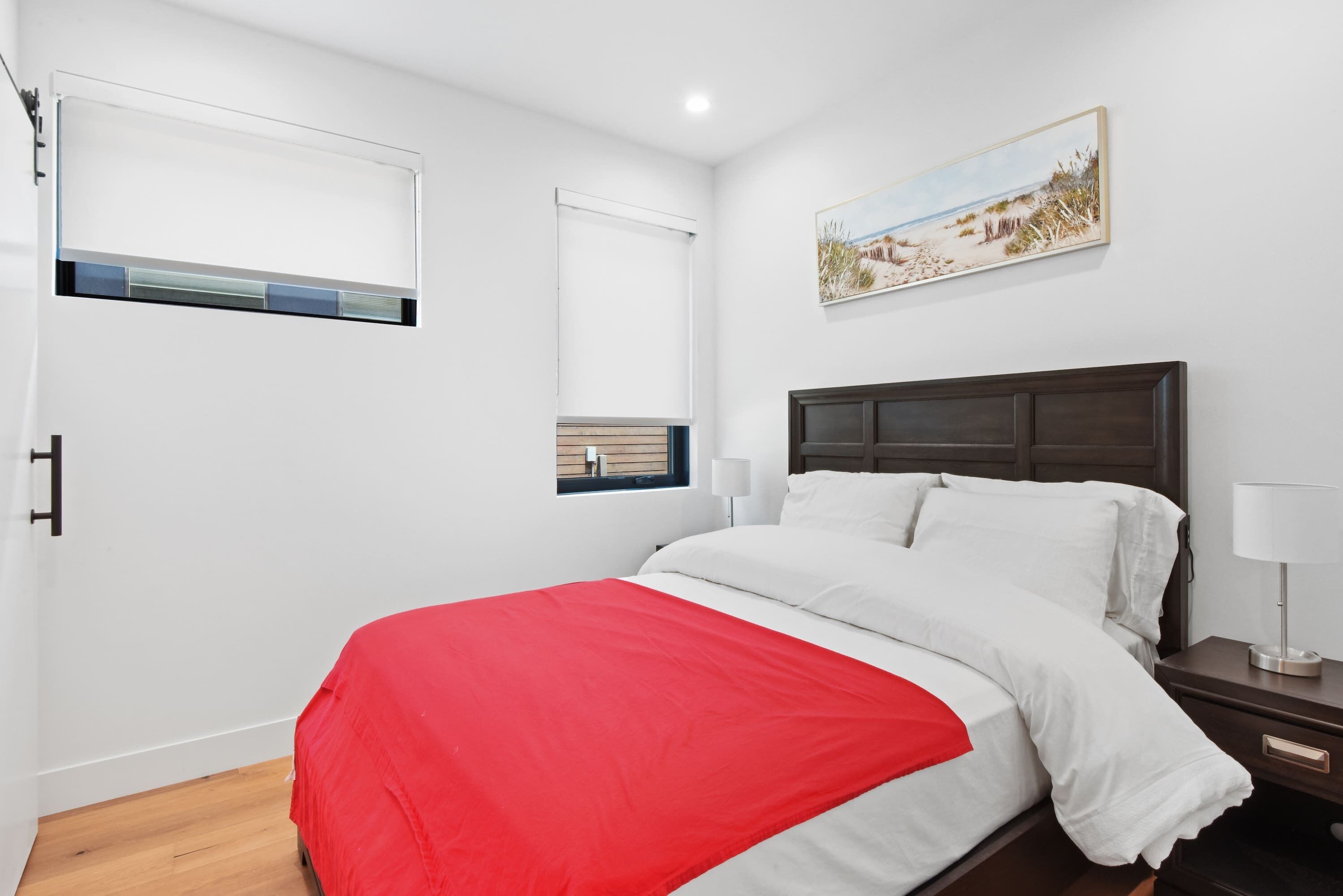 Een slaapkamer met een bed, een nachtkastje, een raam met zonwering en een schilderij aan de muur.