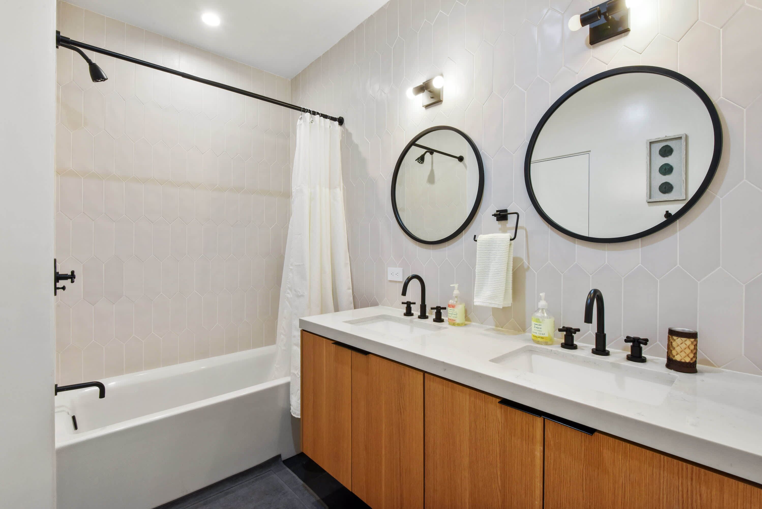 A modern bathroom with a bathtub, two sinks, wooden cabinets, and a large mirror.