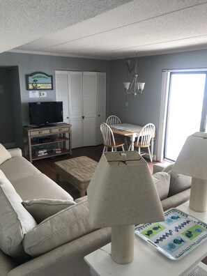 Relax in this inviting living room with a sofa set, dining table, and television, leading to a bright outdoor space.