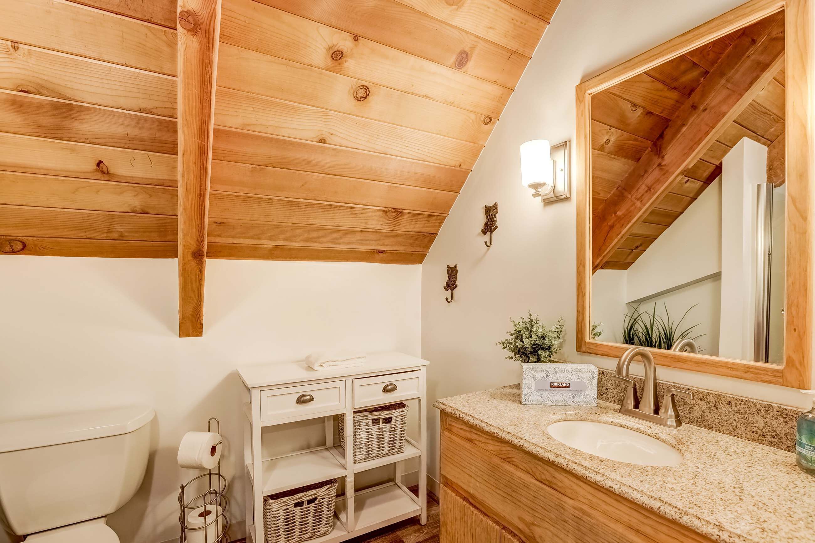 Un baño con techo de madera, tocador blanco, lavamanos y un espejo grande.