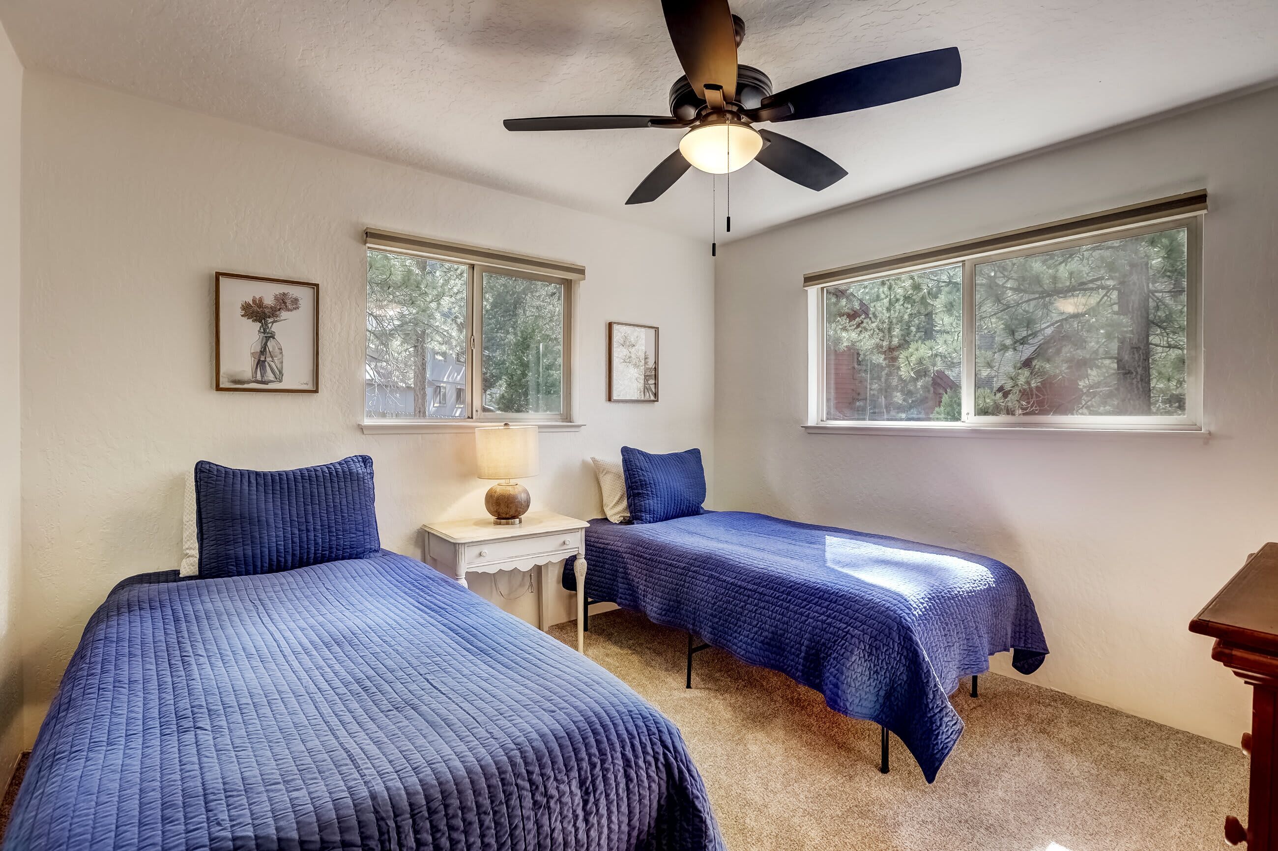 A bedroom with two beds, a ceiling fan, and large windows.