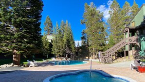 A swimming pool with a wooden deck and lounge chairs, surrounded by trees and a building with a staircase. - St. Anton Getaway - Shared Bbq, Pool & Hot Tub (Mammoth Lakes)