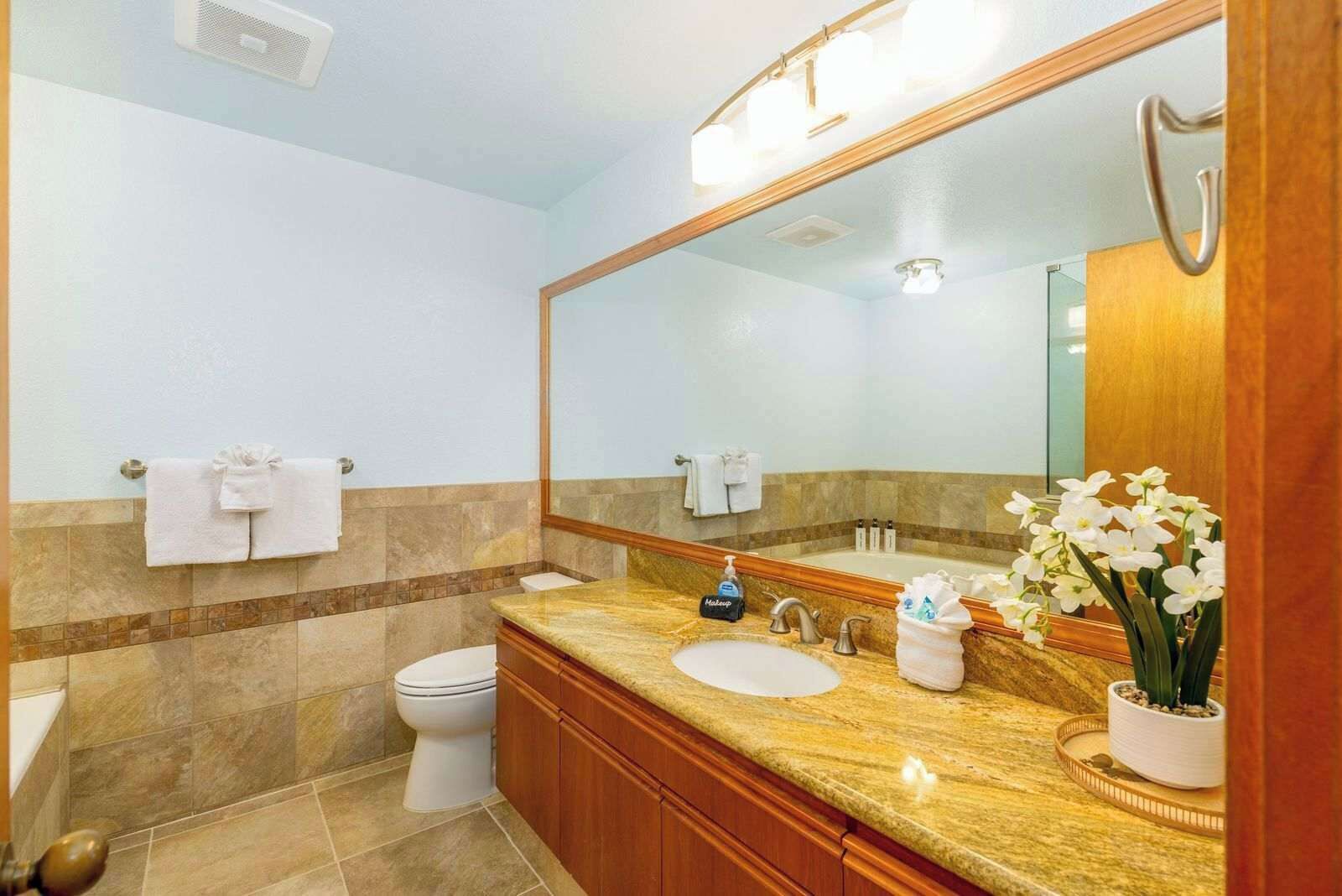 A bathroom with a large mirror, a sink, a toilet, and a shower area.