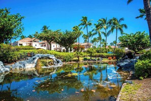 Un resort con un estanque central, palmeras y un edificio de techo con tejas.