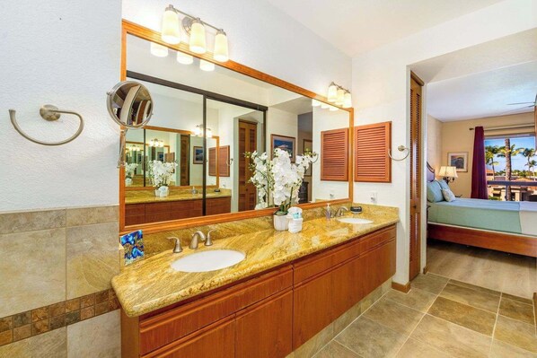A bathroom with a large mirror, two sinks, a vanity with a granite countertop, and a view of a balcony with palm trees. - Shores at Waikoloa Beach Resort 315 (Waikoloa)