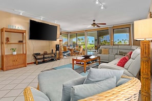 Relax in style with a comfortable seating area featuring a sofa and chair, large windows offering a view of palm trees.