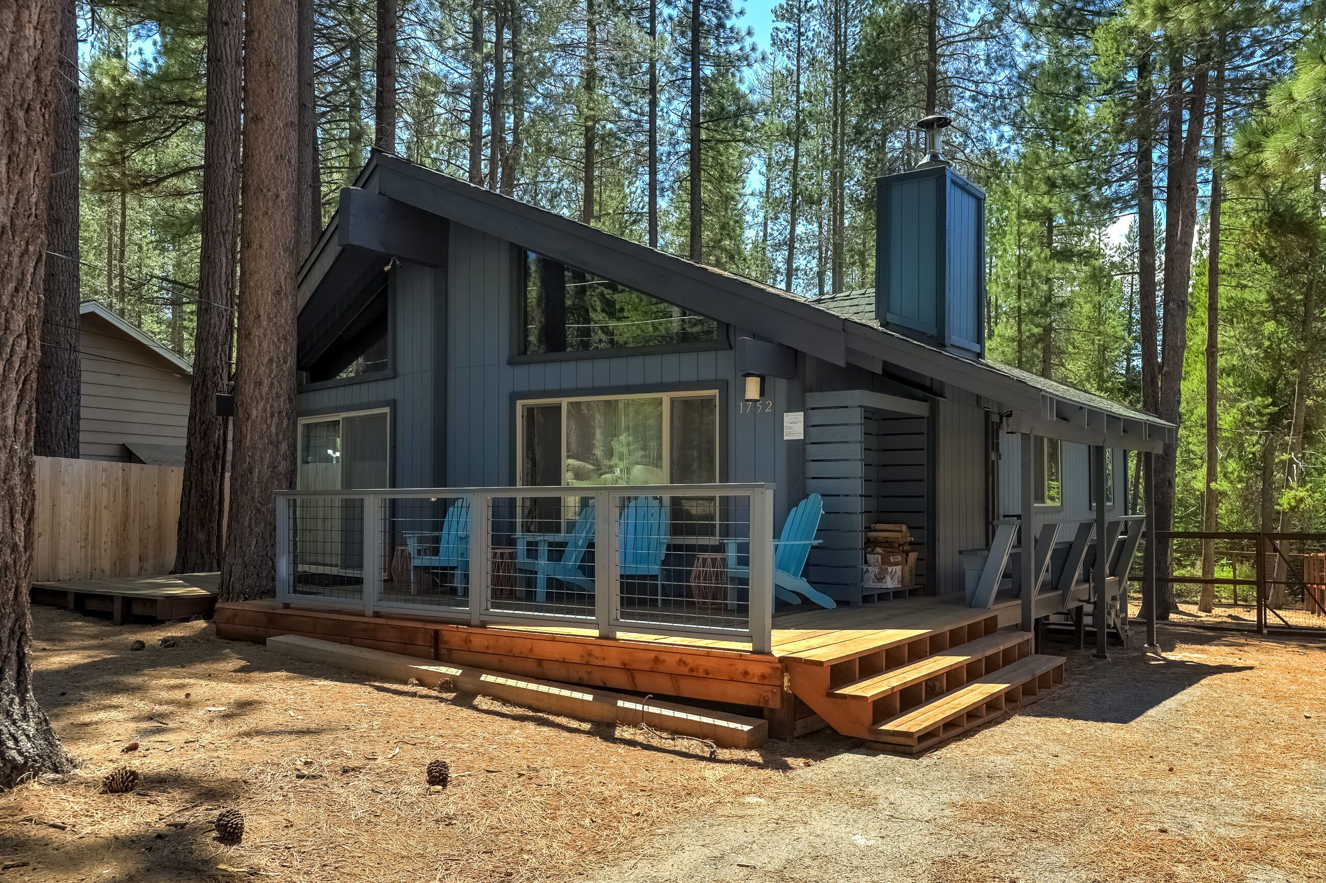 A cabin with a deck, large windows, and a chimney.