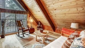 Un dormitorio estilo loft acogedor con techo de madera, una mecedora, una mesita pequeña y una cama con almohadones estampados.