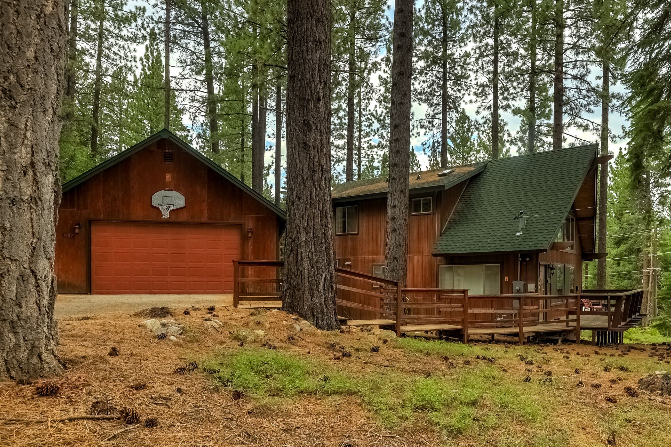 A rustic cabin with a basketball hoop, wooden deck, and a red garage door.